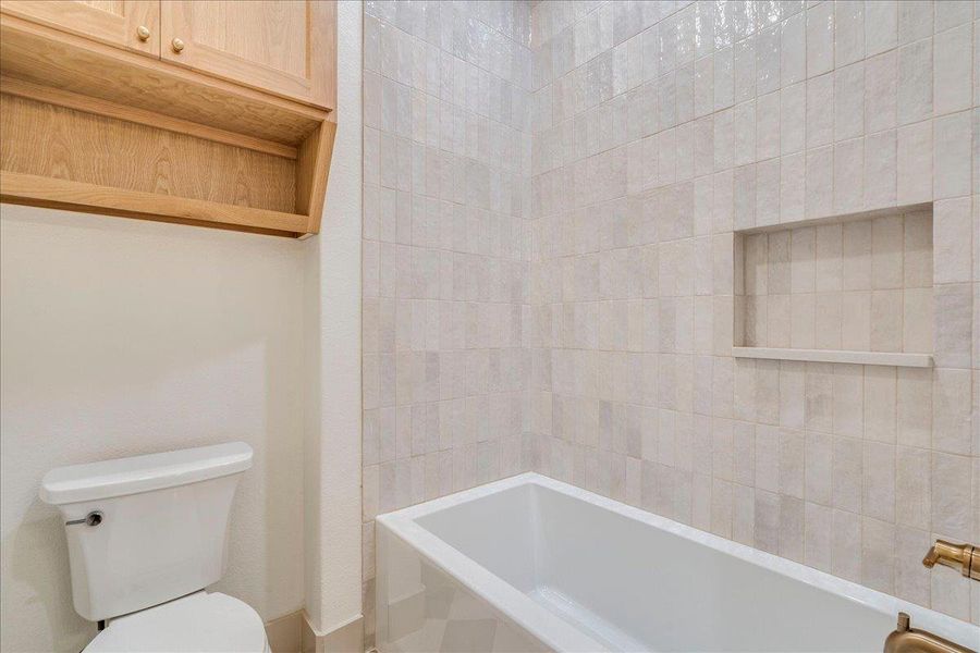 A well-appointed bathroom offers sleek tiling and integrated shelving above the bathtub for convenience.