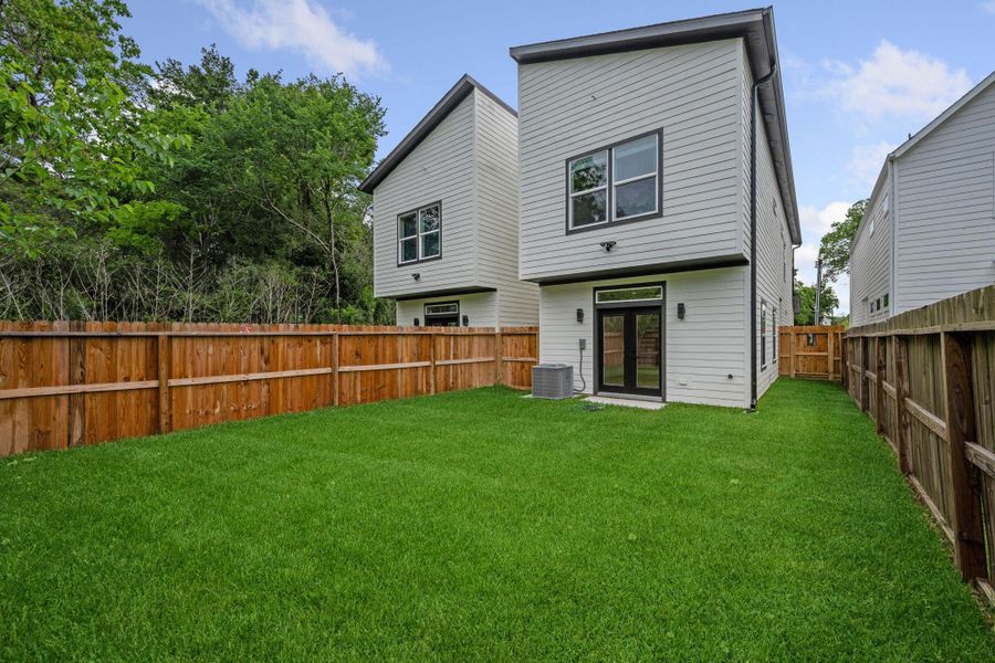 Modern two-story home with a spacious, fenced backyard and lush green lawn, perfect for outdoor activities and privacy.