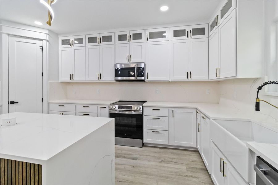 Kitchen with appliances with stainless steel finishes, glass insert cabinets, light stone countertops, white cabinets, and recessed lighting