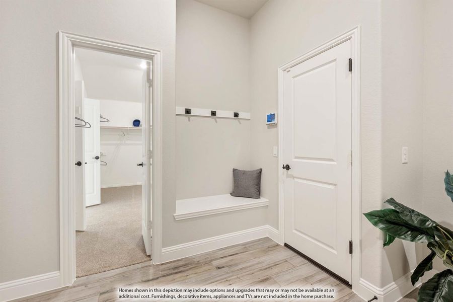 Mudroom with built-in bench, coat hooks, and light wood floors, with walk-in closet visible through doorway Mudroom with built-in bench, coat hooks, and light wood floors, with walk-in closet visible through doorway