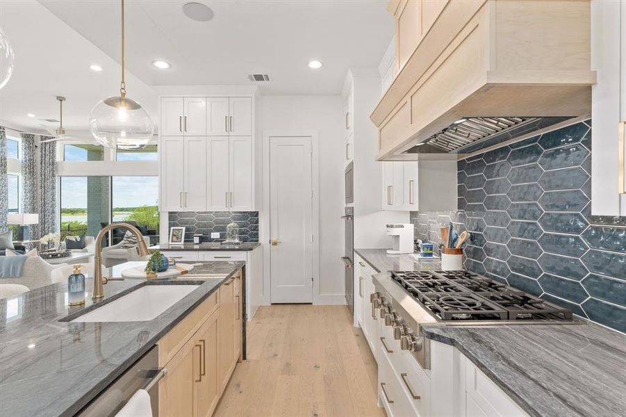 Kitchen with dark stone countertops, decorative light fixtures, premium range hood, appliances with stainless steel finishes, and light wood-type flooring Kitchen with dark stone countertops, decorative light fixtures, premium range hood, appliances with stainless steel finishes, and light wood-type flooring