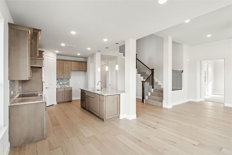 Open kitchen with gray-brown cabinets, center island, and light hardwood floors open to staircase Open kitchen with gray-brown cabinets, center island, and light hardwood floors open to staircase