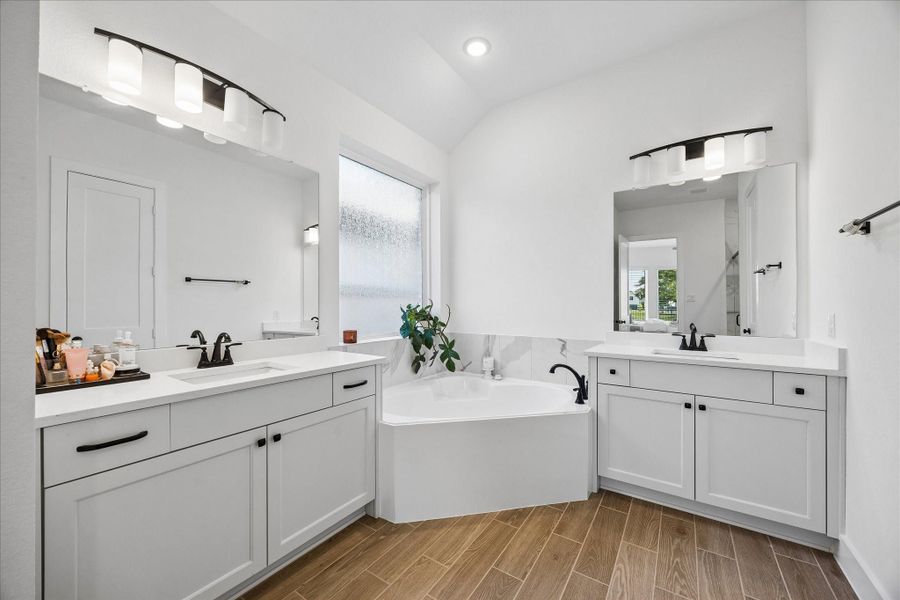 Dual vanity layout with quartz countertops and J Kraft cabinetry offers both style and functionality, paired with matte black fixtures for a clean, modern finish. Corner soaking tub is framed by a frosted window, bringing in natural light while maintaining privacy. Dual vanity layout with quartz countertops and J Kraft cabinetry offers both style and functionality, paired with matte black fixtures for a clean, modern finish. Corner soaking tub is framed by a frosted window, bringing in natural light while maintaining privacy.
