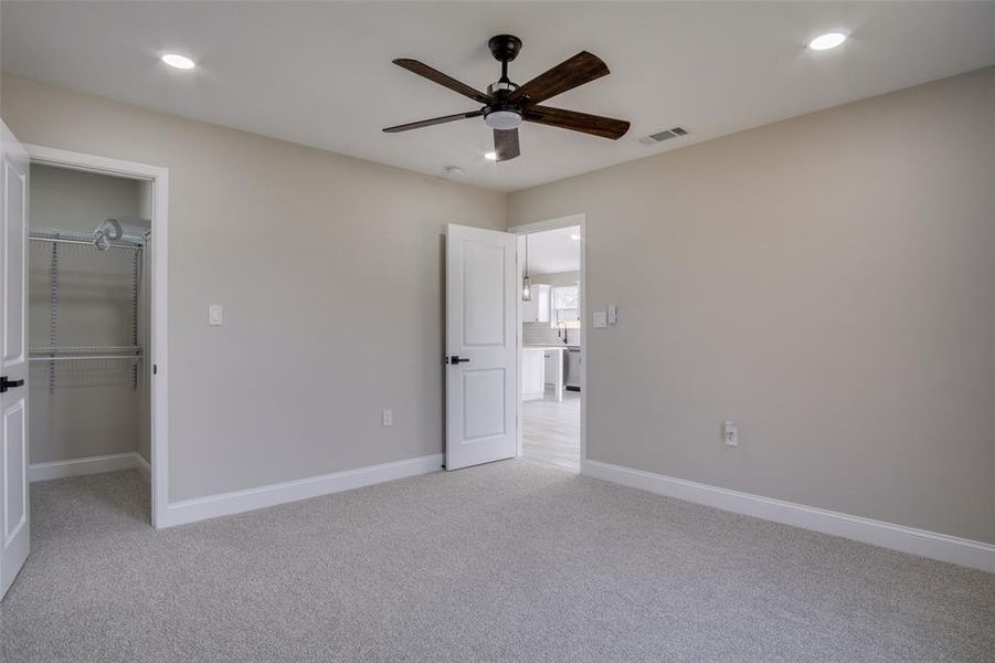 Unfurnished bedroom with a spacious closet, visible vents, baseboards, light colored carpet, and recessed lighting