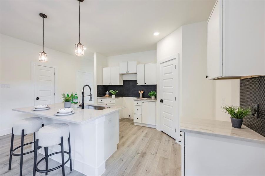 Kitchen with backsplash, an island with sink, light wood finished floors, white cabinetry, and a kitchen breakfast bar