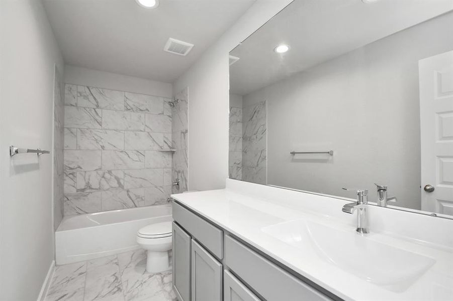 The secondary bath boasts stylish tile flooring, a bath/shower combo with a sleek tile surround, light wood cabinets, and a stunning light countertop. Sample photo of completed home with similar floor plan. As-built interior colors and selections may vary.