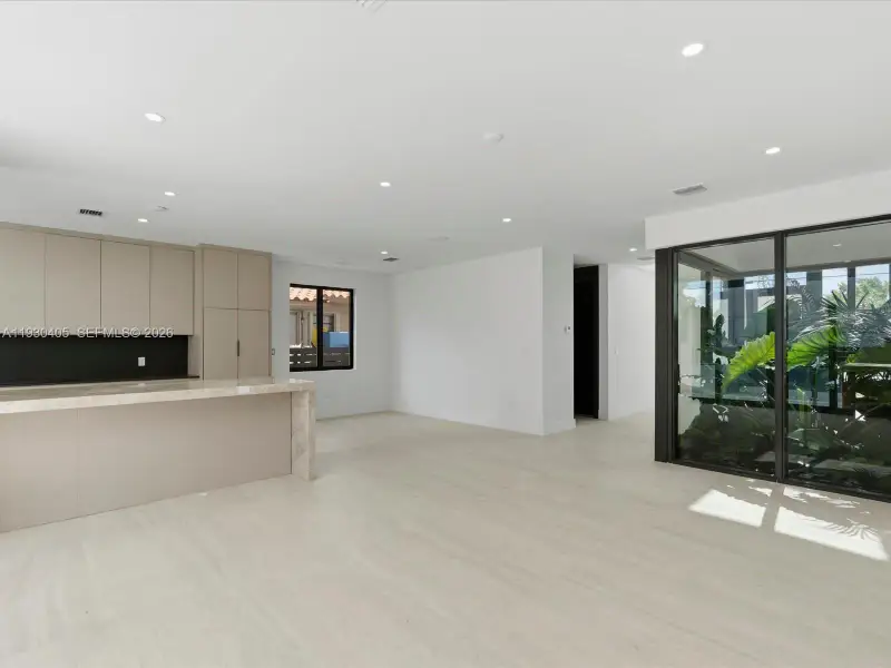 Open-concept area featuring neutral oversized tile flooring, recessed ceiling lighting, kitchen cabinetry with stone-surface counters, and large-format sliding glass doors Open-concept area featuring neutral oversized tile flooring, recessed ceiling lighting, kitchen cabinetry with stone-surface counters, and large-format sliding glass doors