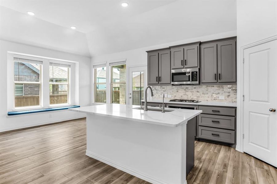 Kitchen featuring a central island with white countertop, gray cabinetry, stainless steel microwave, gas cooktop, and light-toned backsplash