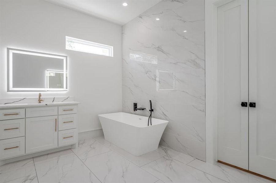 Bathroom with vanity, a freestanding tub, light marble finish flooring, tile walls, and recessed lighting Bathroom with vanity, a freestanding tub, light marble finish flooring, tile walls, and recessed lighting