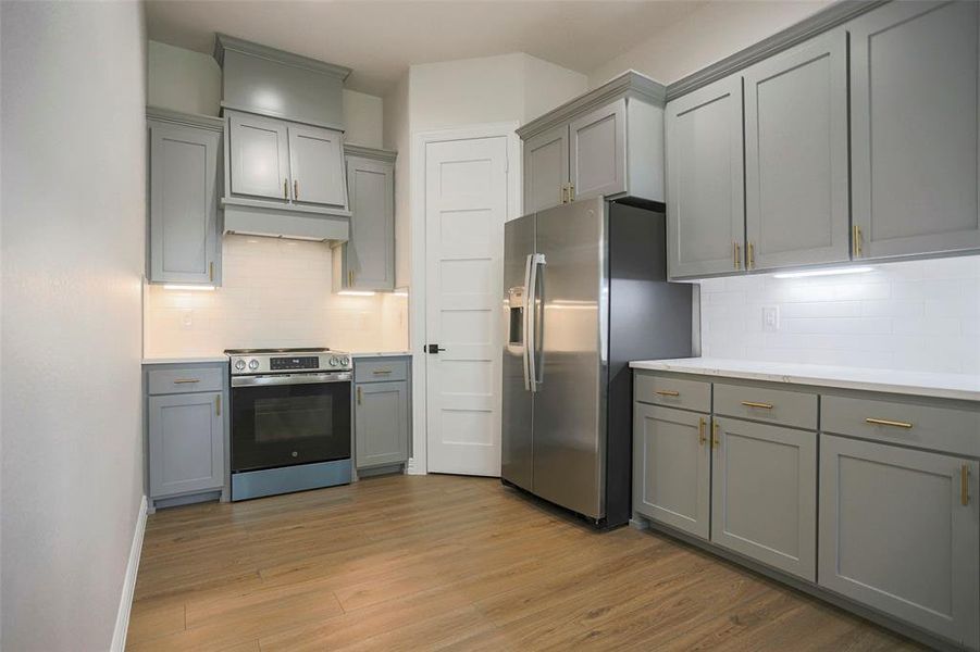 Kitchen with stainless steel appliances, light hardwood / wood-style floors, gray cabinets, and backsplash