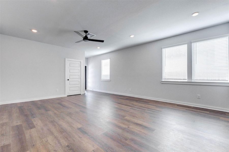 This angle of the living room reveals the natural light pouring in through twin windows, adding warmth to the neutral palette. Luxury vinyl plank floors flow throughout, offering both style and durability in this open-concept space perfect for entertaining or relaxing.