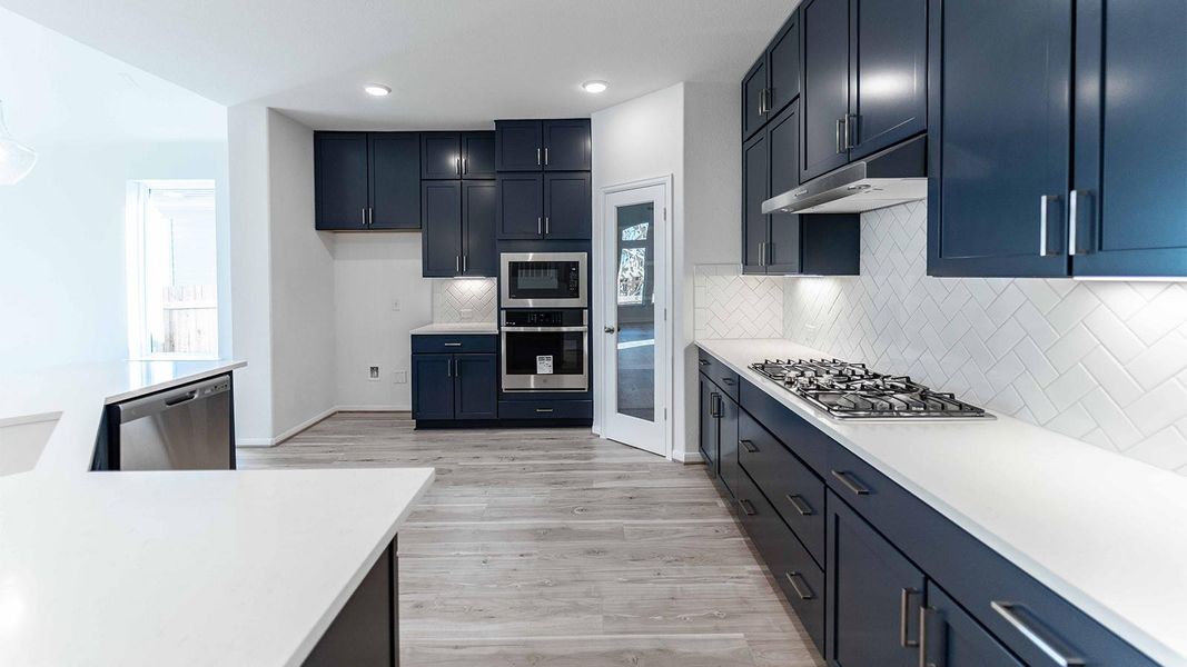 Kitchen with stainless steel appliances, light wood-type flooring, light stone countertops, decorative backsplash, and recessed lighting