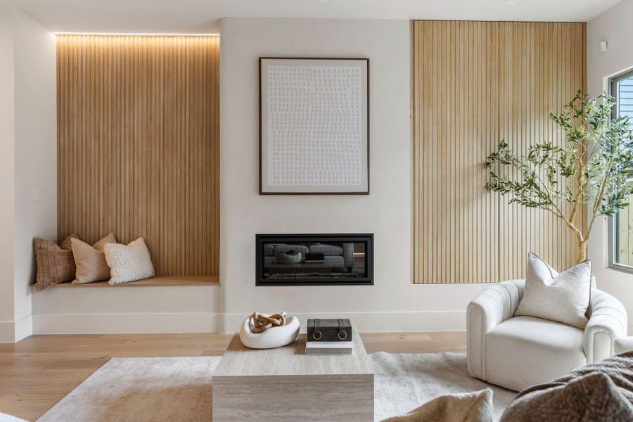 Enter into the living room centered around a gas fireplace finished in custom plaster with seamless cornerless detailing, flanked by a recessed built-in bench seat and a retractable slatted accent wall that discreetly conceals the TV for a sleek, minimal aesthetic. Enter into the living room centered around a gas fireplace finished in custom plaster with seamless cornerless detailing, flanked by a recessed built-in bench seat and a retractable slatted accent wall that discreetly conceals the TV for a sleek, minimal aesthetic.