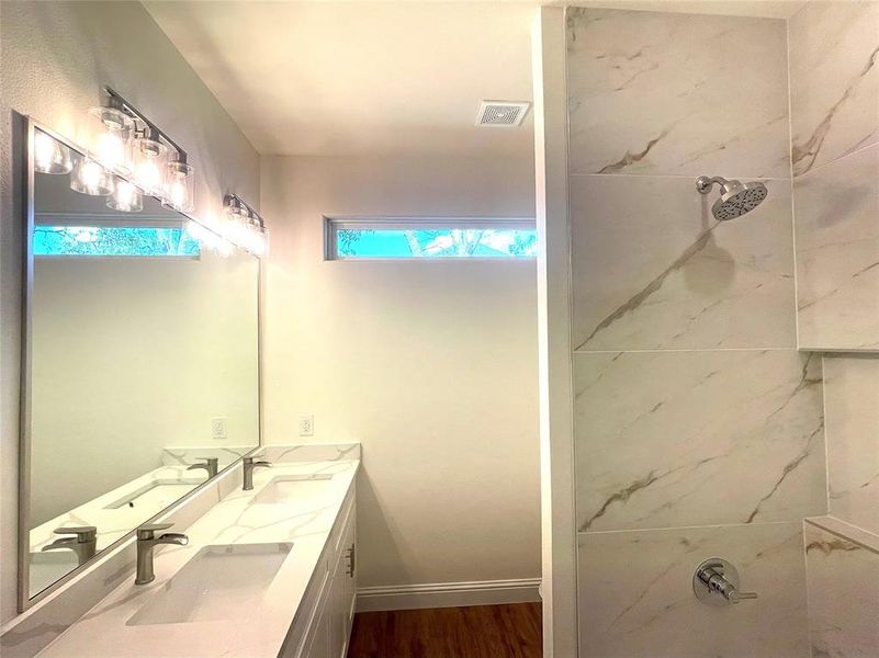 Bathroom with double vanity, hardwood / wood-style floors, and tiled shower