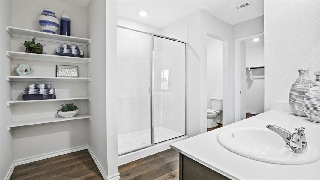 Full bathroom featuring an enclosed shower with sliding glass doors, a single-basin vanity with an integrated sink and chrome faucet, open shelving, and wood-finish flooring