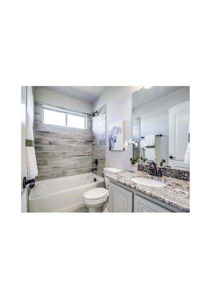 Full bathroom featuring vanity, tiled shower / bath combo, and toilet