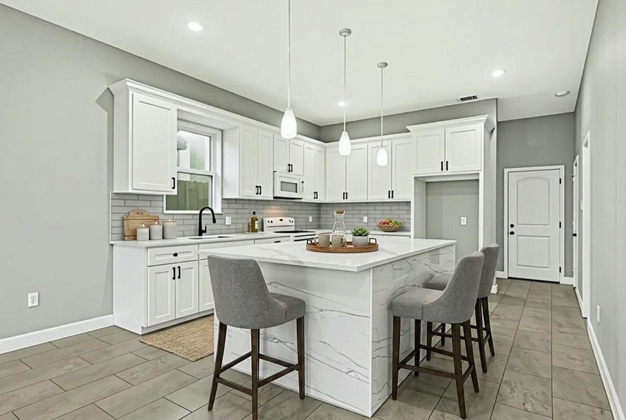 This modern kitchen features sleek white cabinetry, a large island with marble-style countertops, and contemporary pendant lighting. The space is accented by a subway tile backsplash and includes appliances. The neutral tones create a bright and inviting atmosphere, perfect for entertaining.