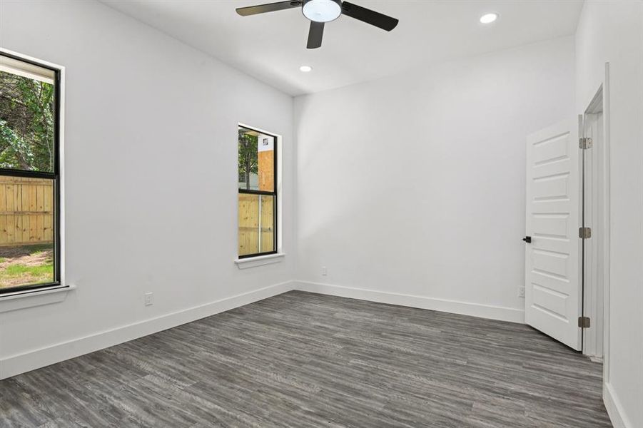 Empty room featuring healthy amount of natural light, a ceiling fan, dark wood-style floors, and recessed lighting Empty room featuring healthy amount of natural light, a ceiling fan, dark wood-style floors, and recessed lighting
