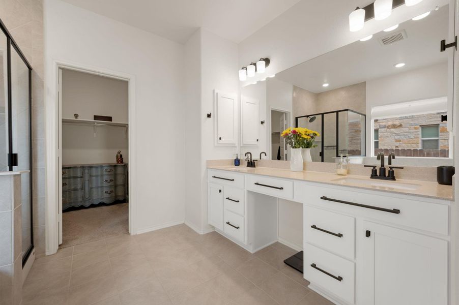 Bathroom with a stall shower, double vanity, a spacious closet, and light tile patterned floors