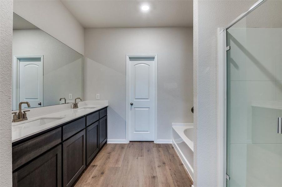 Full bath with double vanity, a garden tub, a shower stall, and light wood-style floors