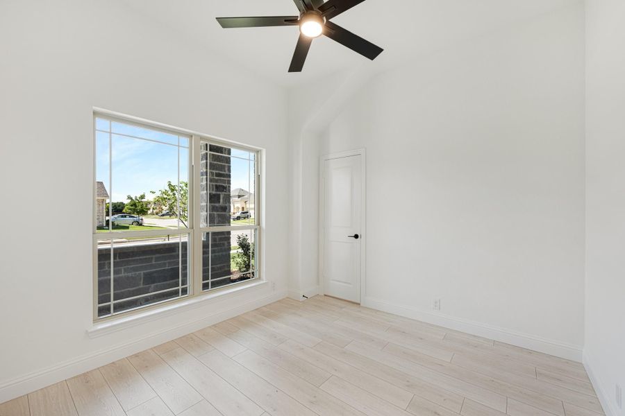 Empty bedroom with vaulted ceiling, ceiling fan, large window, and light wood floors