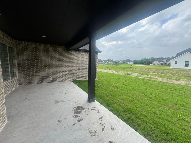 Covered concrete patio with recessed lighting, dark brick exterior, and a dark support pillar