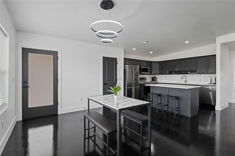 Kitchen with appliances with stainless steel finishes, tasteful backsplash, a breakfast bar area, hanging light fixtures, and a kitchen island