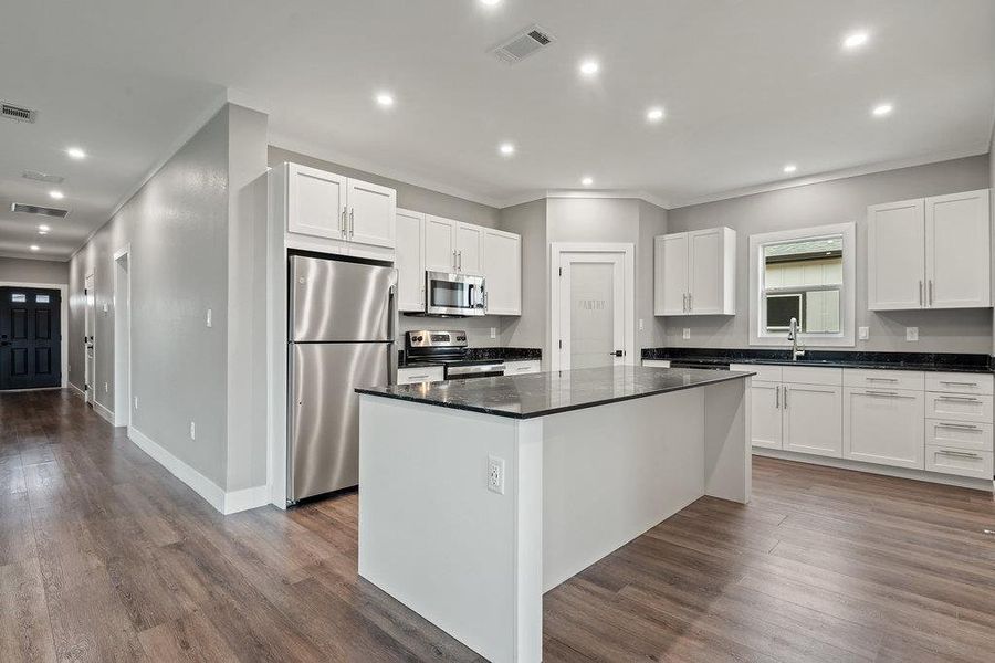 Kitchen with appliances with stainless steel finishes, white cabinetry, dark stone counters, a kitchen island, and dark wood-style flooring