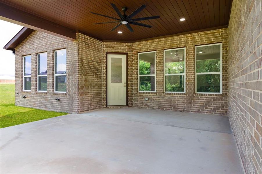 Expansive covered patio featuring a concrete surface, brick exterior, wood-finish ceiling, and a ceiling fan with integrated lighting Expansive covered patio featuring a concrete surface, brick exterior, wood-finish ceiling, and a ceiling fan with integrated lighting
