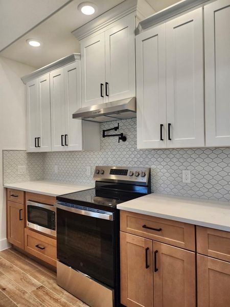 Kitchen with stainless steel appliances, tasteful backsplash, white cabinets, under cabinet range hood, and recessed lighting