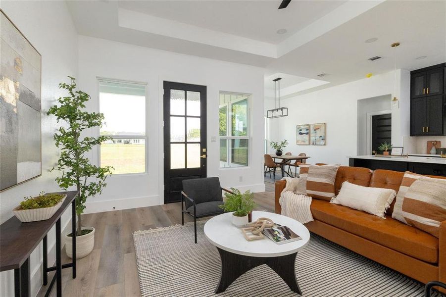 Living room with light wood-type flooring, a tray ceiling, and plenty of natural light