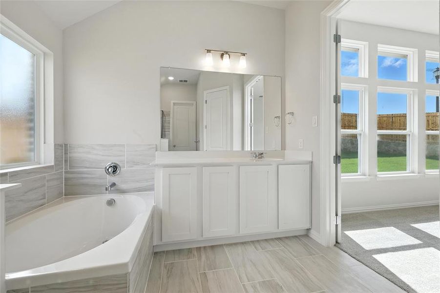 Full bath featuring plenty of natural light, vanity, a garden tub, and lofted ceiling