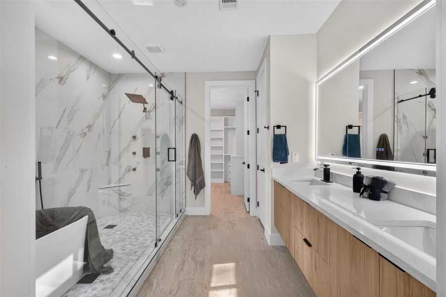 Luxurious bathroom featuring a spacious glass-enclosed shower, elegant marble accents, and a sleek dual-sink vanity with modern lighting.