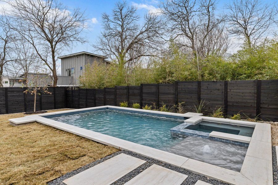 View of swimming pool with a fenced backyard and a pool with connected hot tub