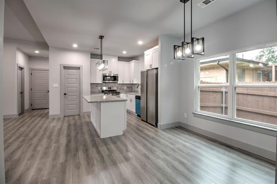 Kitchen featuring a center island, white cabinetry, backsplash, appliances with stainless steel finishes, and decorative light fixtures Kitchen featuring a center island, white cabinetry, backsplash, appliances with stainless steel finishes, and decorative light fixtures