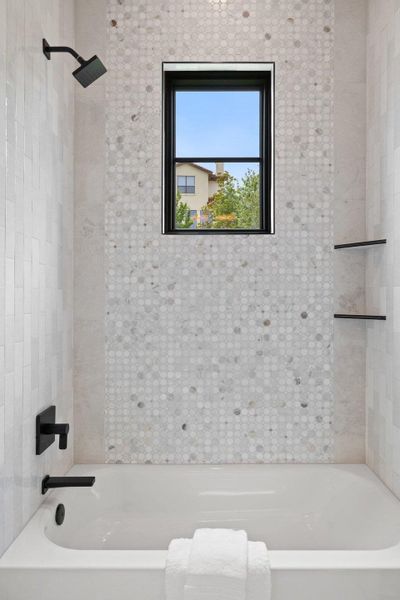 Bathtub with white subway tile surround and mosaic tile accent wall