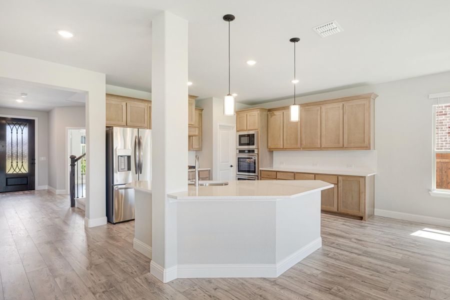Open kitchen with large island, light wood cabinets, stainless steel appliances, and pendant lights over light hardwood floors