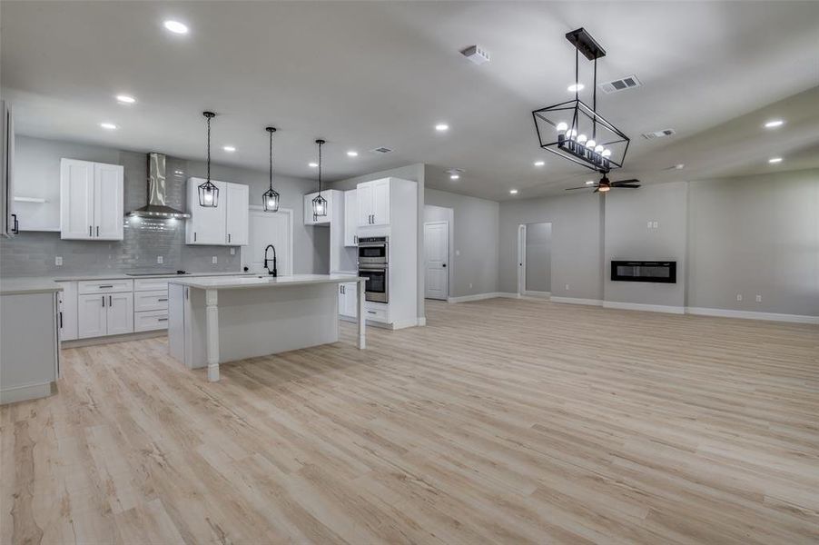 Kitchen featuring hanging light fixtures, open floor plan, decorative backsplash, a center island with sink, and light wood-style floors Kitchen featuring hanging light fixtures, open floor plan, decorative backsplash, a center island with sink, and light wood-style floors