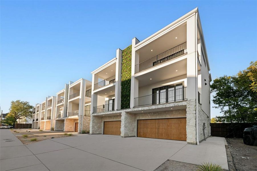 View of front facade with a balcony, stucco siding, stone siding, a garage, and concrete driveway