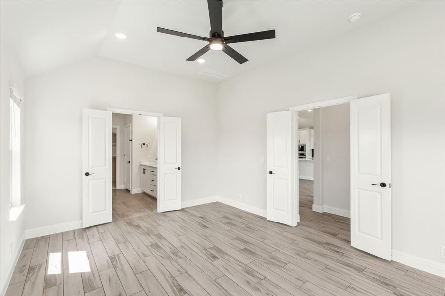 Empty bedroom with light wood floors, black ceiling fan, and two open doors leading to bathroom and hallway