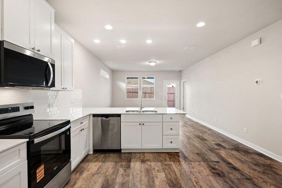 Kitchen with stainless steel appliances, a peninsula, white cabinets, dark wood finished floors, and recessed lighting