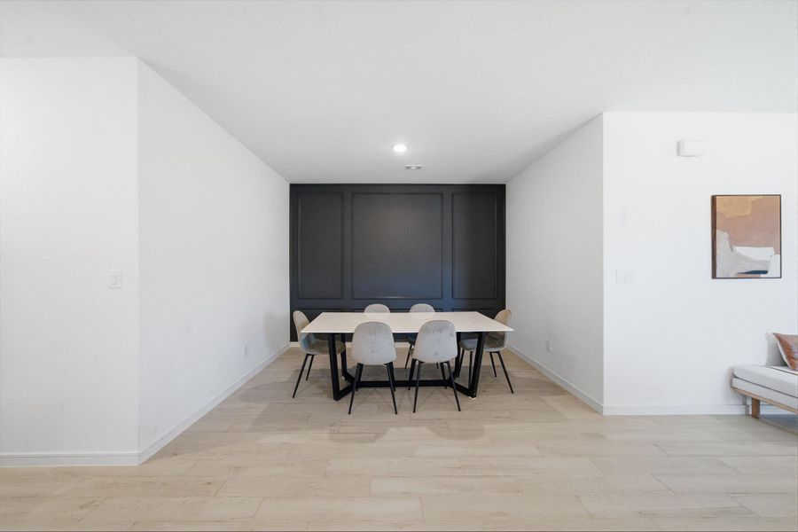 This dining area features a modern, minimalist design with a sleek black accent wall. The space is bright and open, with light wood look tile flooring and neutral walls.