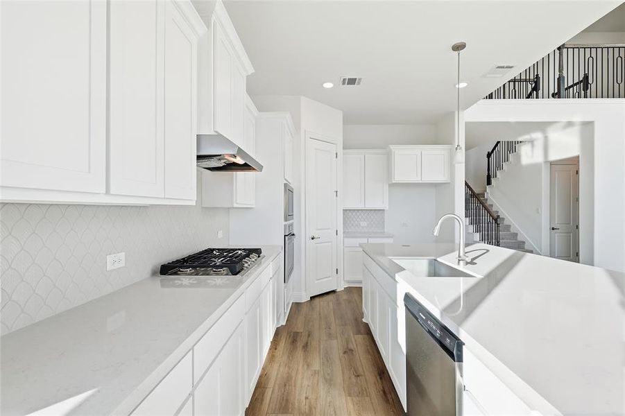 Kitchen featuring white cabinets, stainless steel appliances, light wood-type flooring, decorative backsplash, and light stone counters Kitchen featuring white cabinets, stainless steel appliances, light wood-type flooring, decorative backsplash, and light stone counters