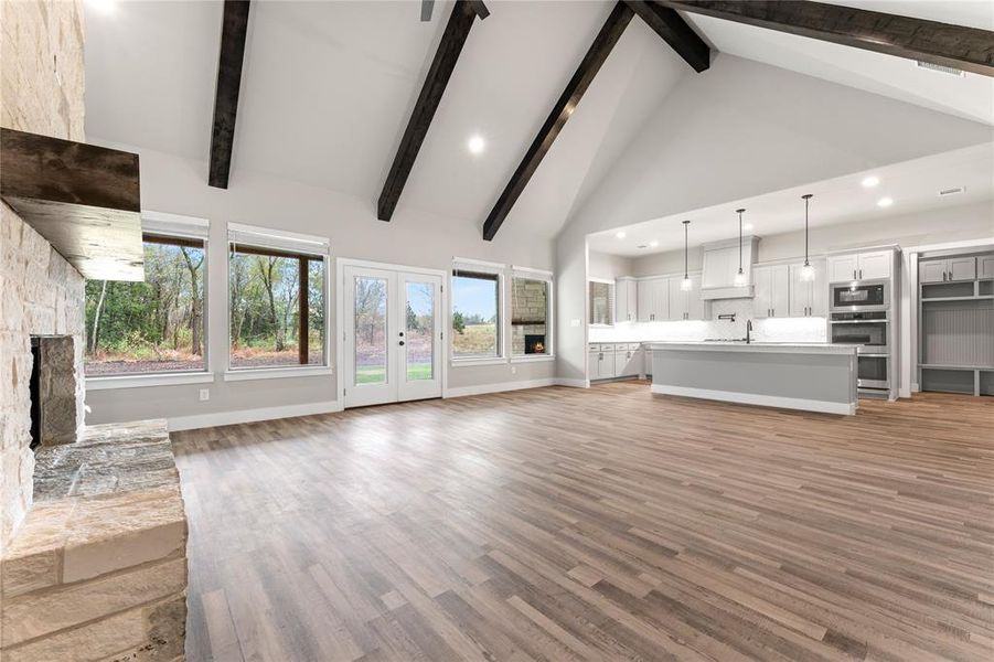 Unfurnished living room with sink, beam ceiling, high vaulted ceiling, a stone fireplace, and light hardwood / wood-style flooring