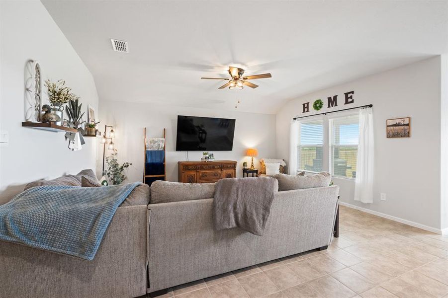 Living room featuring ceiling fan, lofted ceiling, and light tile patterned flooring