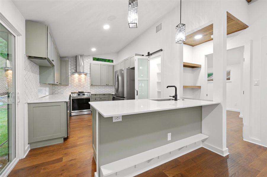 Kitchen featuring appliances with stainless steel finishes, wall chimney exhaust hood, gray cabinets, a peninsula, and decorative backsplash