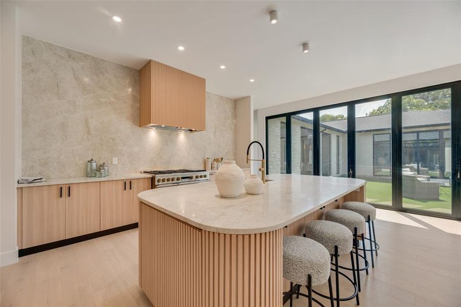 Kitchen with a center island with sink, light hardwood / wood-style flooring, range with two ovens, and decorative backsplash