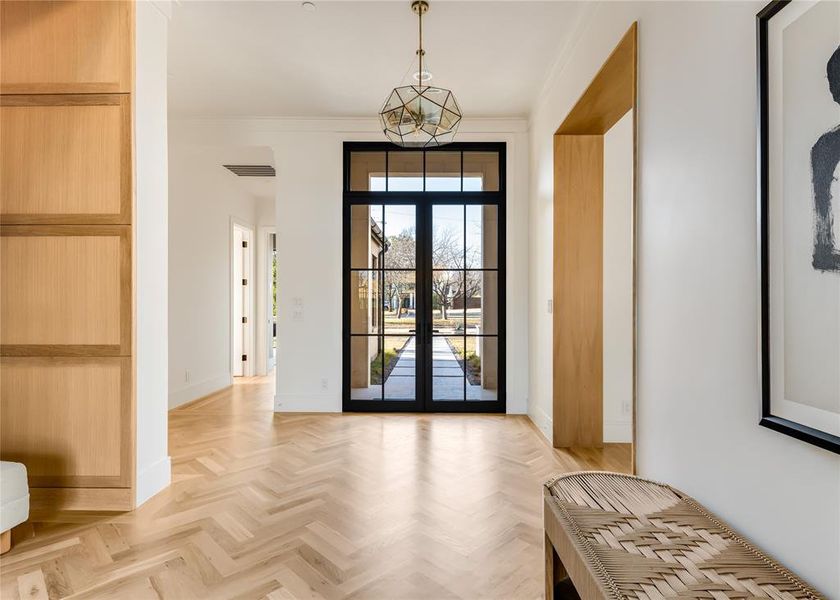 Entryway with french doors, a notable chandelier, ornamental molding, and light parquet floors