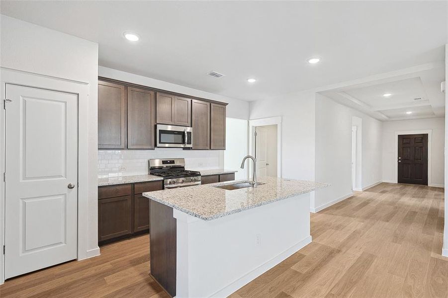 Kitchen with light hardwood / wood-style flooring, appliances with stainless steel finishes, light stone countertops, sink, and tasteful backsplash