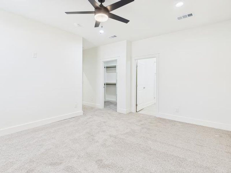 Unfurnished bedroom featuring a walk in closet, light colored carpet, and a ceiling fan Unfurnished bedroom featuring a walk in closet, light colored carpet, and a ceiling fan